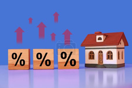 Mortgage rate rising illustrated by upward arrows and percent signs. House model and wooden cubes on table