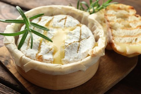 Lecker gebackener Brie-Käse, Brot und Rosmarin auf Holzbrett, Nahaufnahme