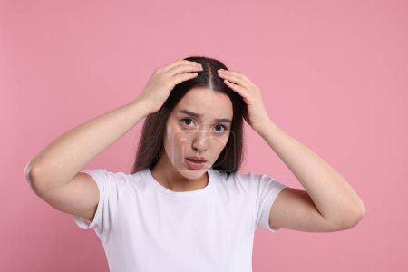 Téléchargez les photos : Triste femme examinant ses cheveux et son cuir chevelu sur fond rose. Problème de pellicules - en image libre de droit