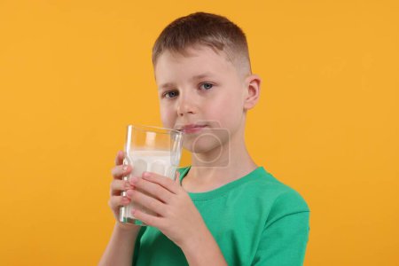 Téléchargez les photos : Mignon garçon avec un verre de lait frais sur fond orange - en image libre de droit