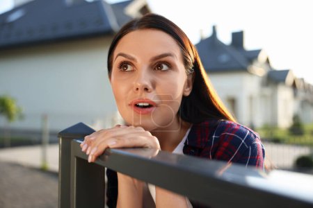 Photo for Concept of private life. Curious young woman spying on neighbours over fence outdoors - Royalty Free Image