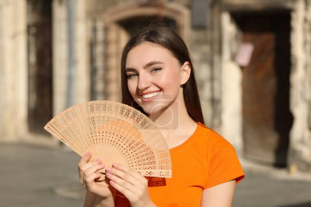 Mujer feliz sosteniendo ventilador de mano en la calle de la ciudad