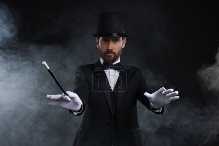 Magician holding wand in smoke on black background