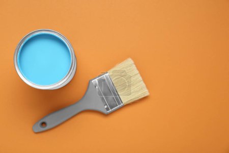 Peut de peinture bleu clair et pinceau sur fond orange pâle, pose à plat. Espace pour le texte