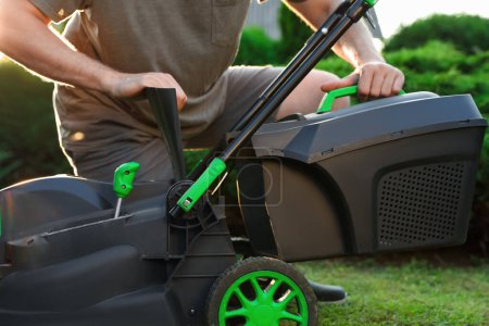 Cleaning lawn mower. Man detaching grass catcher from device in garden, closeup