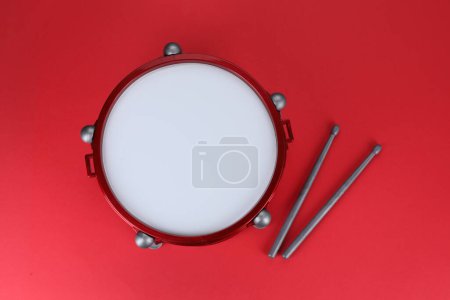 Drum and sticks on red background, top view. Percussion musical instrument