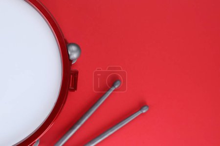 Drum and sticks on red background, top view with space for text. Percussion musical instrument