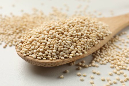 Photo for Spoon with dry quinoa seeds on white table, closeup - Royalty Free Image