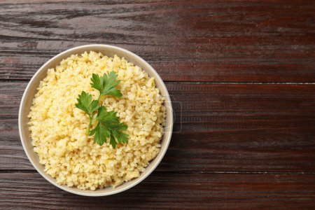 Delicious bulgur with parsley in bowl on wooden table, top view. Space for text
