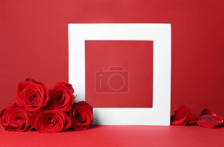 Foto de Elegante presentación para el producto. Marco, hermosas rosas y pétalos sobre fondo rojo, espacio para el texto - Imagen libre de derechos