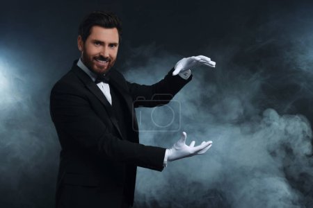 Happy magician holding something in smoke on dark background