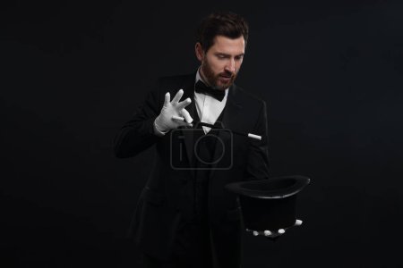 Magicien montrant tour de magie avec chapeau haut de forme sur fond noir