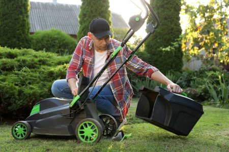 Cleaning lawn mower. Man detaching grass catcher from device in garden