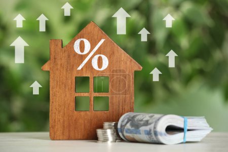 Steigende Hypothekenzinsen illustriert durch Aufwärtspfeile und Prozentzeichen. Hausmodell und Geld auf dem Tisch