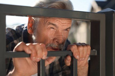 Concept of private life. Curious senior man spying on neighbours over fence outdoors, closeup