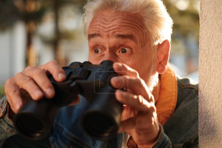 Konzept des Privatlebens. Neugieriger Senior mit Fernglas spioniert Nachbarn im Freien aus, Nahaufnahme