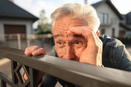 Téléchargez les photos : Concept de vie privée. Homme âgé curieux espionnant les voisins au-dessus de la clôture à l'extérieur, gros plan - en image libre de droit