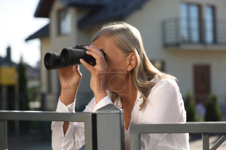 Konzept des Privatlebens. Neugierige Seniorin mit Fernglas spioniert Nachbarn über Gartenzaun aus