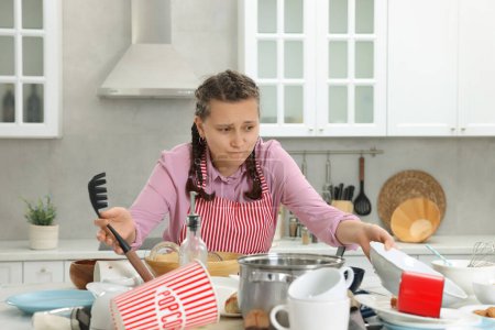 Mujer molesta en la cocina desordenada. Mucha vajilla sucia y utensilios en la mesa