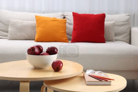 Photo for Red apples with book on nesting tables and comfortable sofa in living room. Interior design - Royalty Free Image