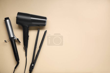 Téléchargez les photos : Fer à friser, lisseur et sèche-cheveux sur fond beige, pose plate. Espace pour le texte - en image libre de droit