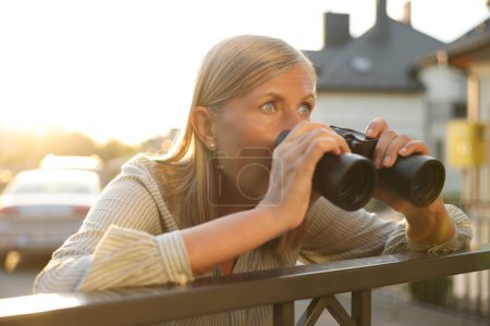 Konzept des Privatlebens. Neugierige Seniorin mit Fernglas spioniert Nachbarn über Gartenzaun aus