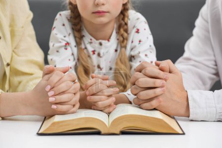 Photo for Girl and her godparents praying over Bible together at table indoors, closeup - Royalty Free Image