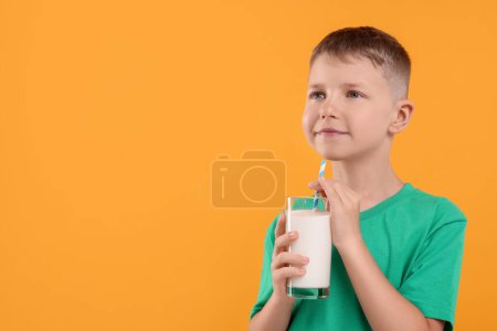 Téléchargez les photos : Garçon mignon avec verre de lait frais sur fond orange, espace pour le texte - en image libre de droit