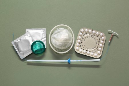 Píldoras anticonceptivas, condones y dispositivo intrauterino sobre fondo de oliva, planas. Diferentes métodos anticonceptivos