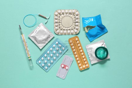 Píldoras anticonceptivas, condones, dispositivo intrauterino y termómetro sobre fondo turquesa, planas. Diferentes métodos anticonceptivos
