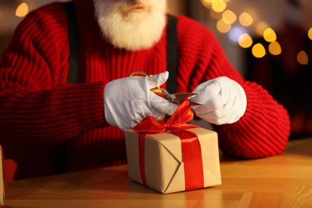 Foto de Santa Claus atando arco en caja de regalo en su lugar de trabajo en la habitación decorada para Navidad, primer plano - Imagen libre de derechos