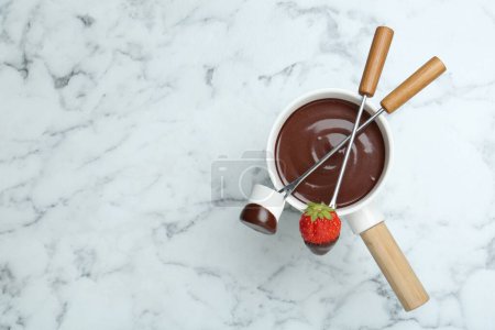 Foto de Fondue olla de chocolate derretido, tenedores con malvavisco dulce y fresa fresca en la mesa de mármol blanco, la puesta plana. Espacio para texto - Imagen libre de derechos