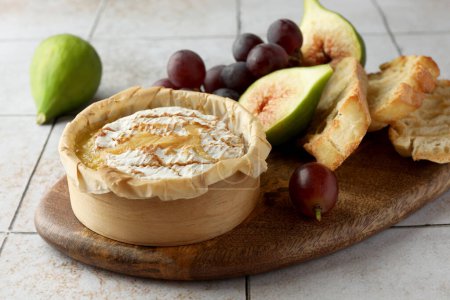 Leckerer gebackener Brie-Käse und Produkte auf hellem Kacheltisch