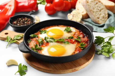 Photo for Delicious shakshuka in frying pan and products on white table, closeup - Royalty Free Image