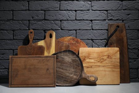 Foto de Diferentes tablas de cortar de madera en la mesa gris cerca de pared de ladrillo oscuro - Imagen libre de derechos