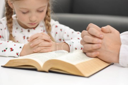 Mädchen und ihr Patenonkel beten gemeinsam an einem Tisch im Haus über die Bibel, selektiver Fokus