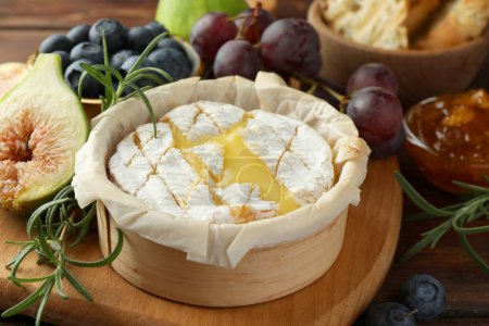 Lecker gebackener Brie-Käse und Produkte auf Holztisch, Nahaufnahme