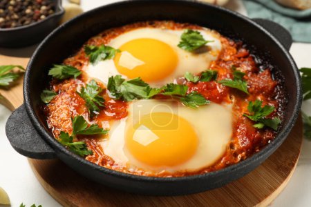 Delicious shakshuka in frying pan on white table, closeup