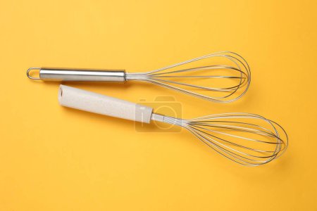Two metal whisks on yellow background, top view