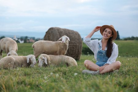 Smiling woman with sheep on pasture at farm