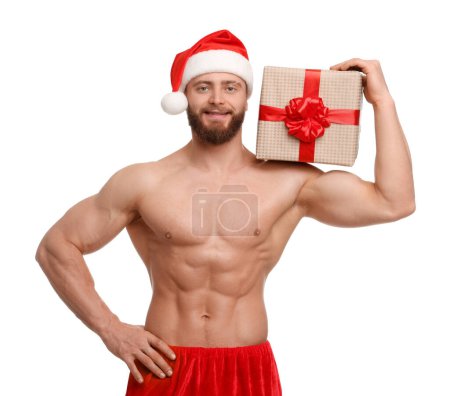Photo for Attractive young man with muscular body in Santa hat holding Christmas gift box on white background - Royalty Free Image