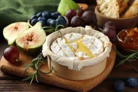 Leckerer gebackener Brie-Käse und Produkte auf Holztisch