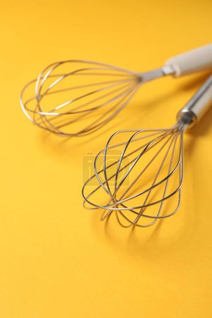 Two metal whisks on yellow background, closeup