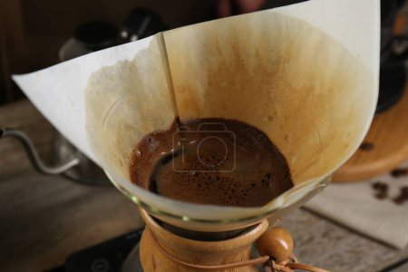 Brewing aromatic coffee in glass chemex coffeemaker with paper filter on table, closeup