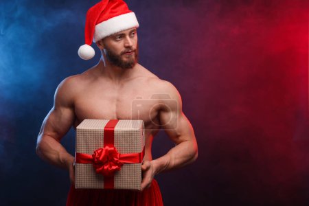 Photo for Attractive young man with muscular body holding Christmas gift box on color background, space for text - Royalty Free Image