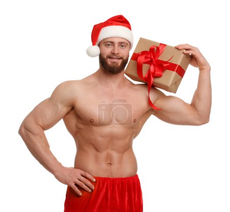 Photo for Attractive young man with muscular body in Santa hat holding Christmas gift box on white background - Royalty Free Image