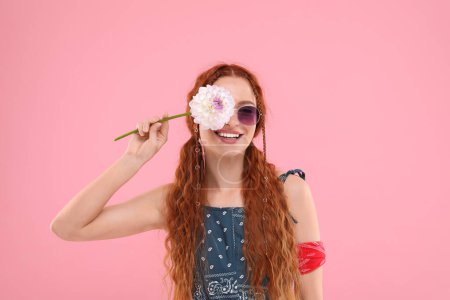 Stilvolle junge Hippie-Frau mit Dahlienblüte auf rosa Hintergrund