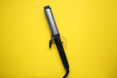 Hair curling iron on yellow background, top view