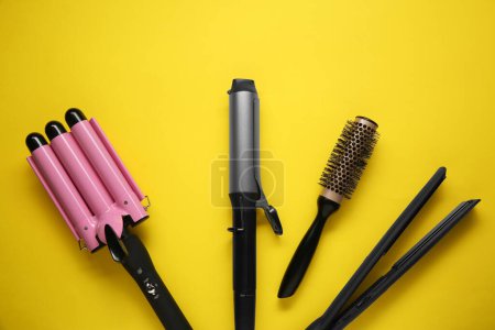Différents fers à friser, lisseur et brosse ronde sur fond jaune, pose plate