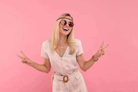 Retrato de mujer hippie sonriente mostrando signos de paz sobre fondo rosa